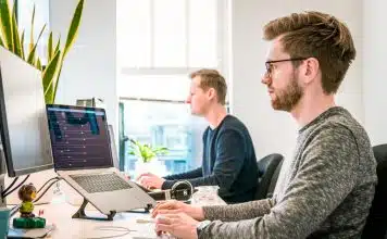 man sitting on chair wearing gray crew-neck long-sleeved shirt using Apple Magic Keyboard